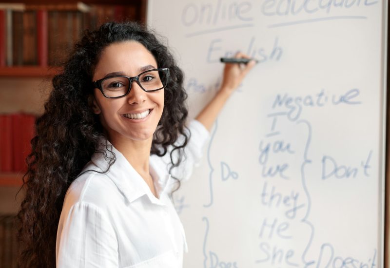 english-teacher-standing-at-board-explaining-lesson-to-students.jpg